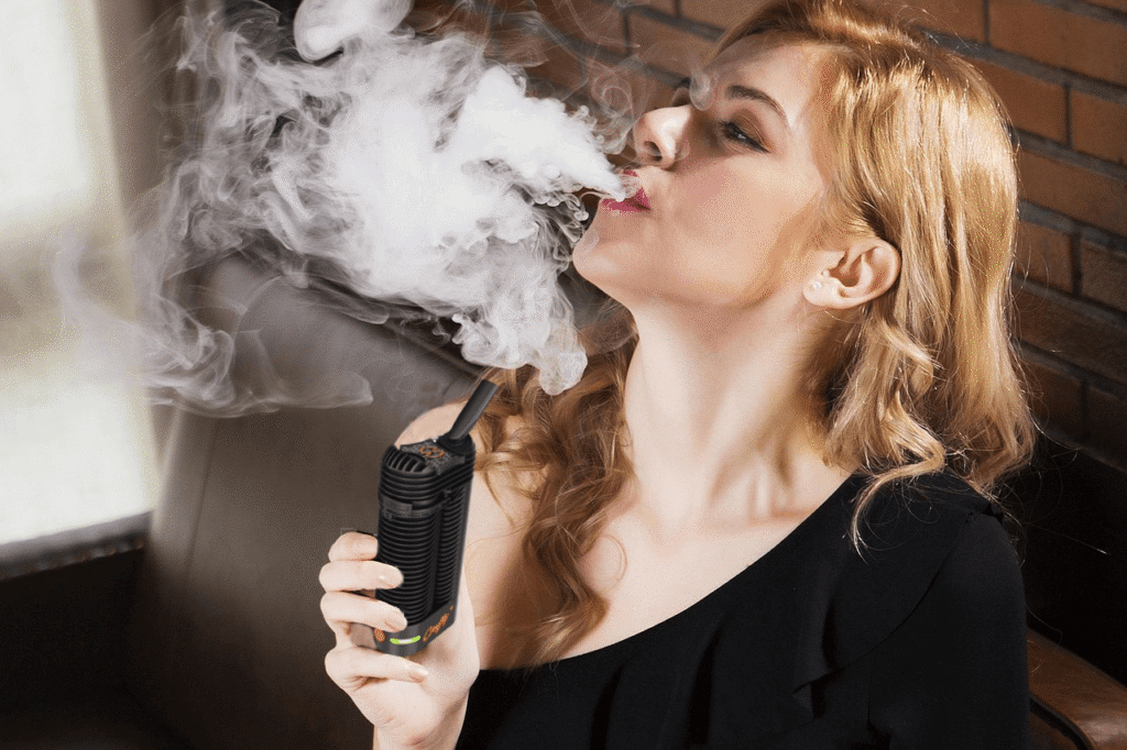 Blonde woman blowing a cloud of vapor after hitting a Storz & Bickel Crafty Plus portable vaporizer.